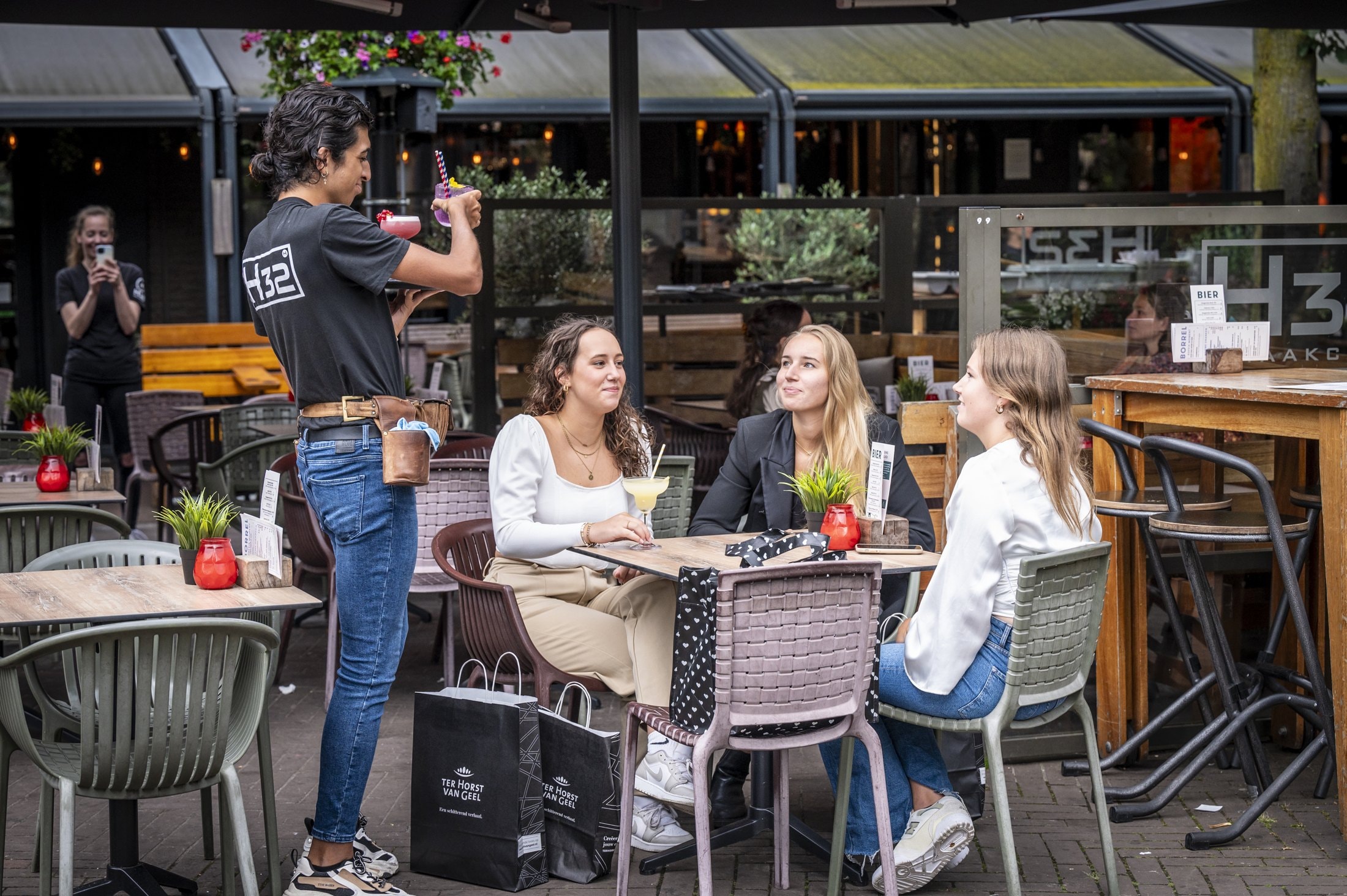 Een horecamedewerker serveert drankjes aan drie bezoekers op een terras in Oss.