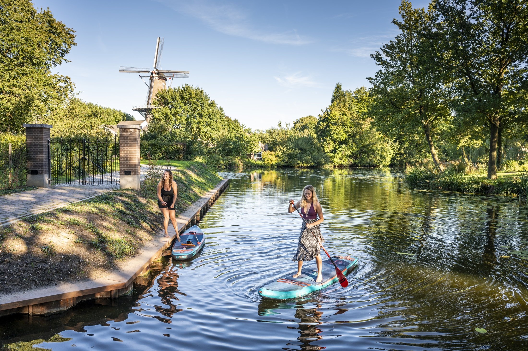 Twee suppers op het water in Ravenstein, met groen en een molen op de achtergrond.