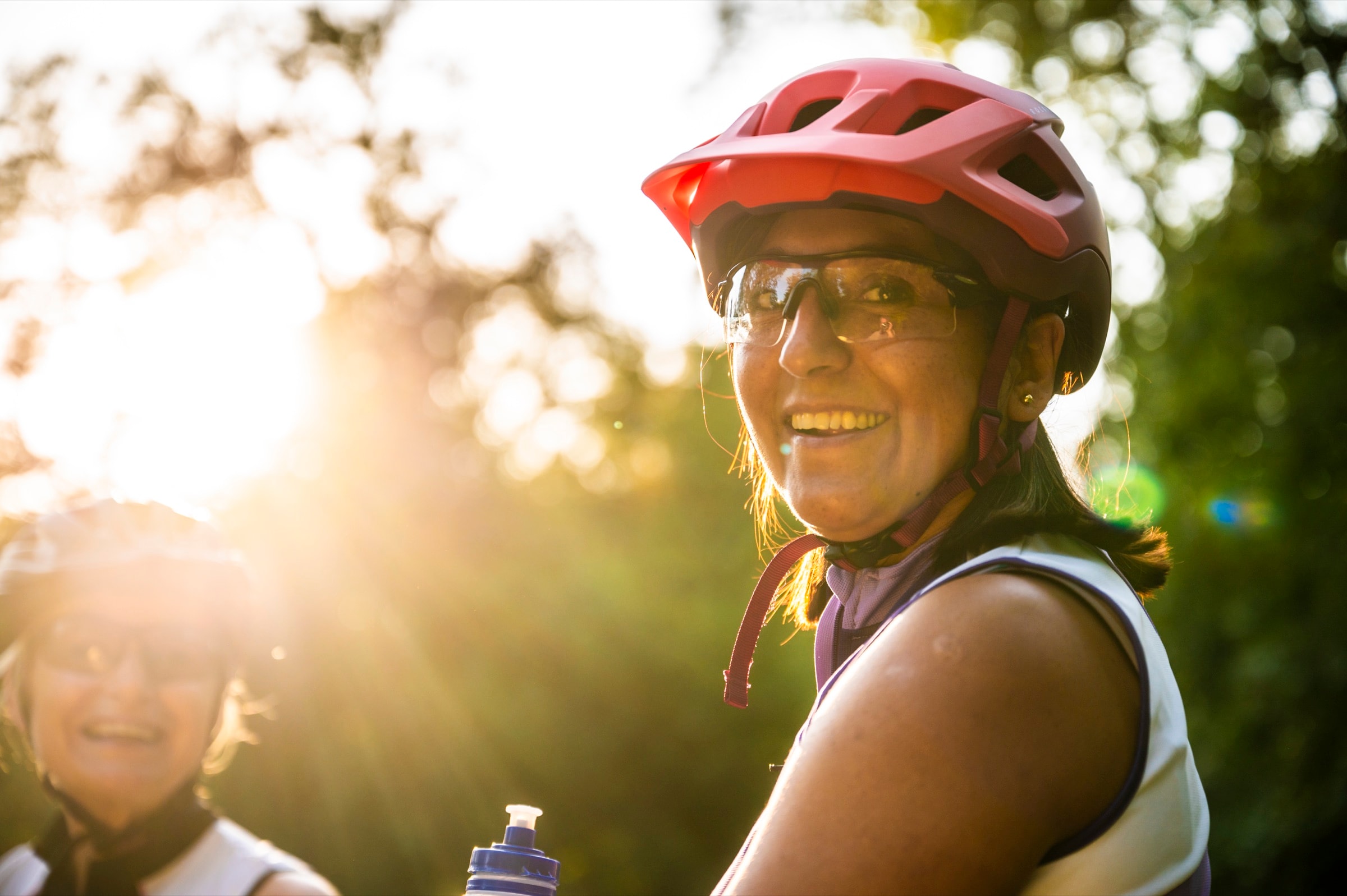 Een lachende fietser met helm, in tegenlicht tussen de bomen.